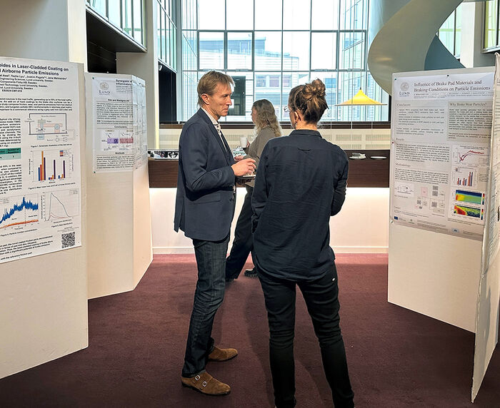 Two people talking in front of large posters. Photo.