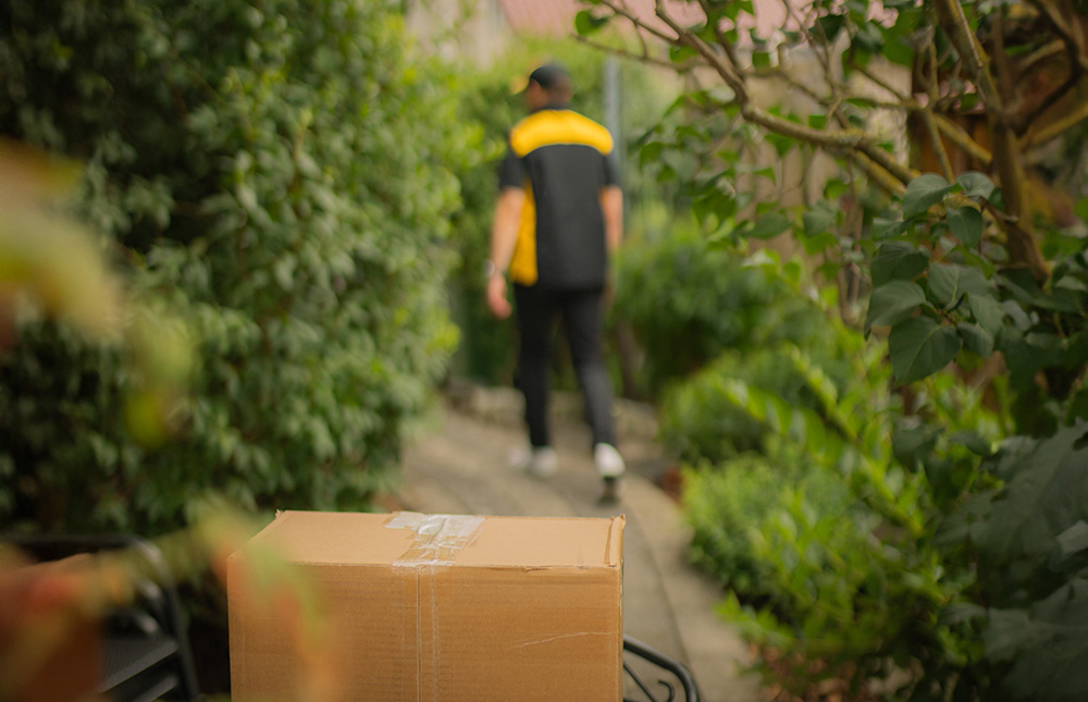 A package in a bicycle basket in the foreground. In the background a man. Photo.