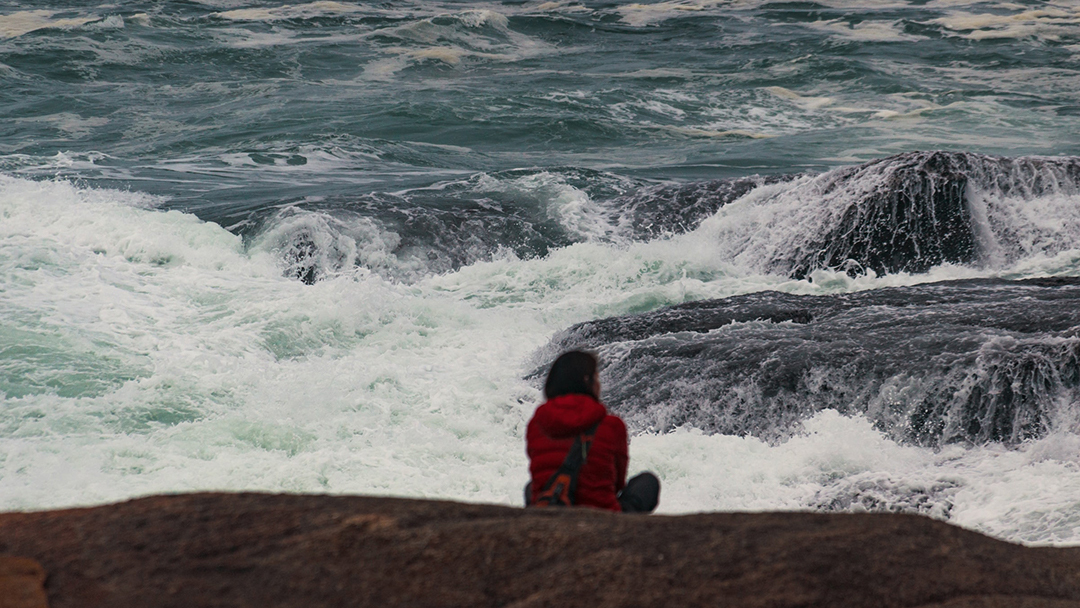 a person sitting in the foreground looking out at a stormy sea. Photo. 