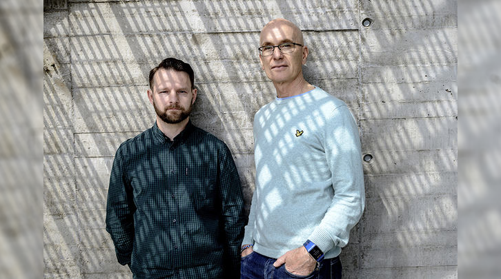 two men standing against a concrete wall. Photo. 