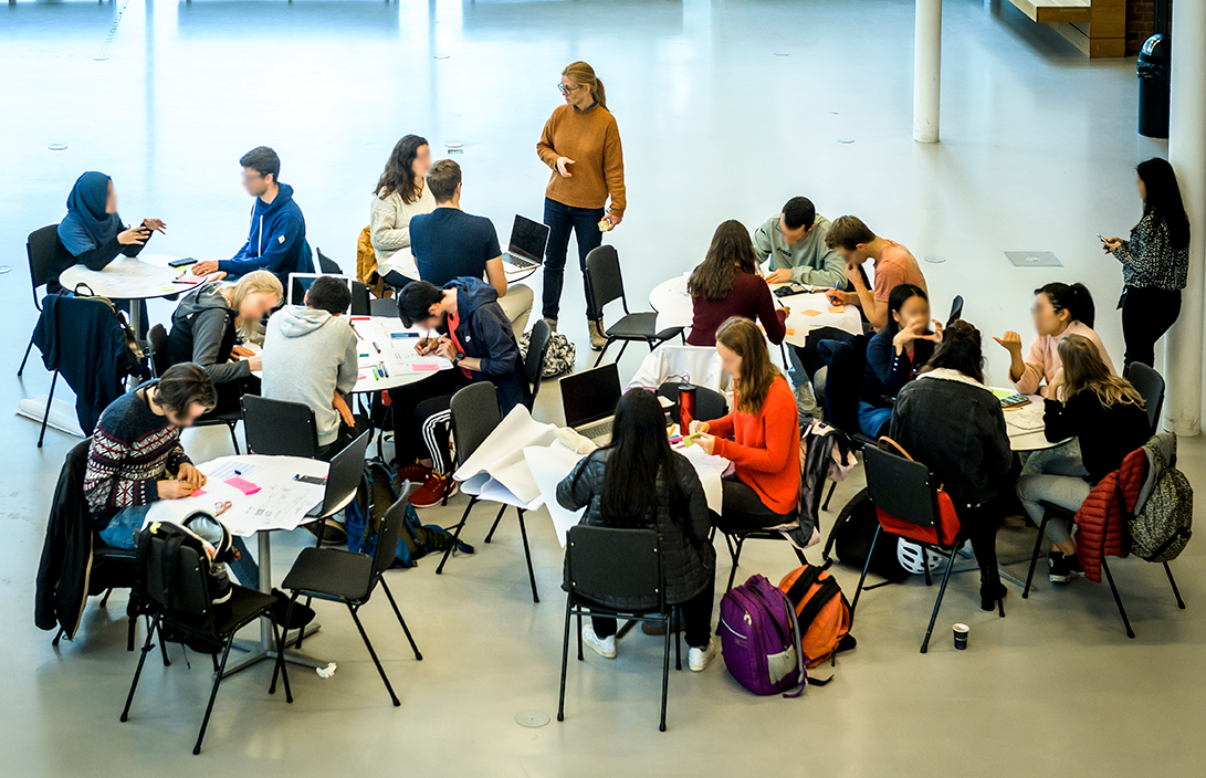 People in a room sitting around different tables working together. Photo.